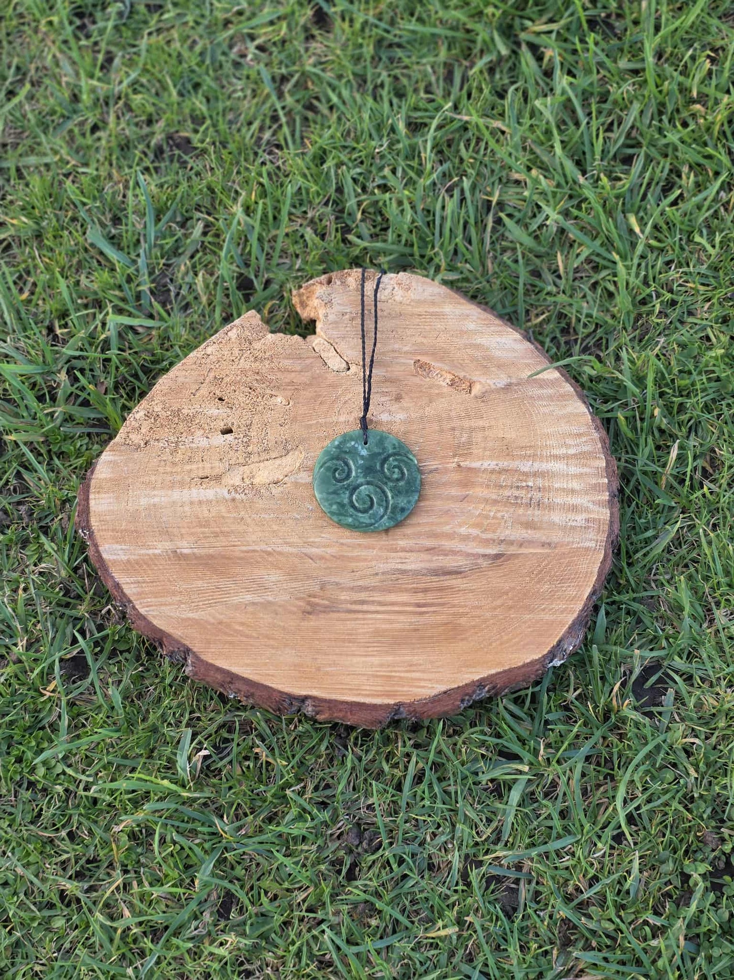 Circular pounamu (greenstone) necklace on black braiding with three koru (spirals) carved decoration