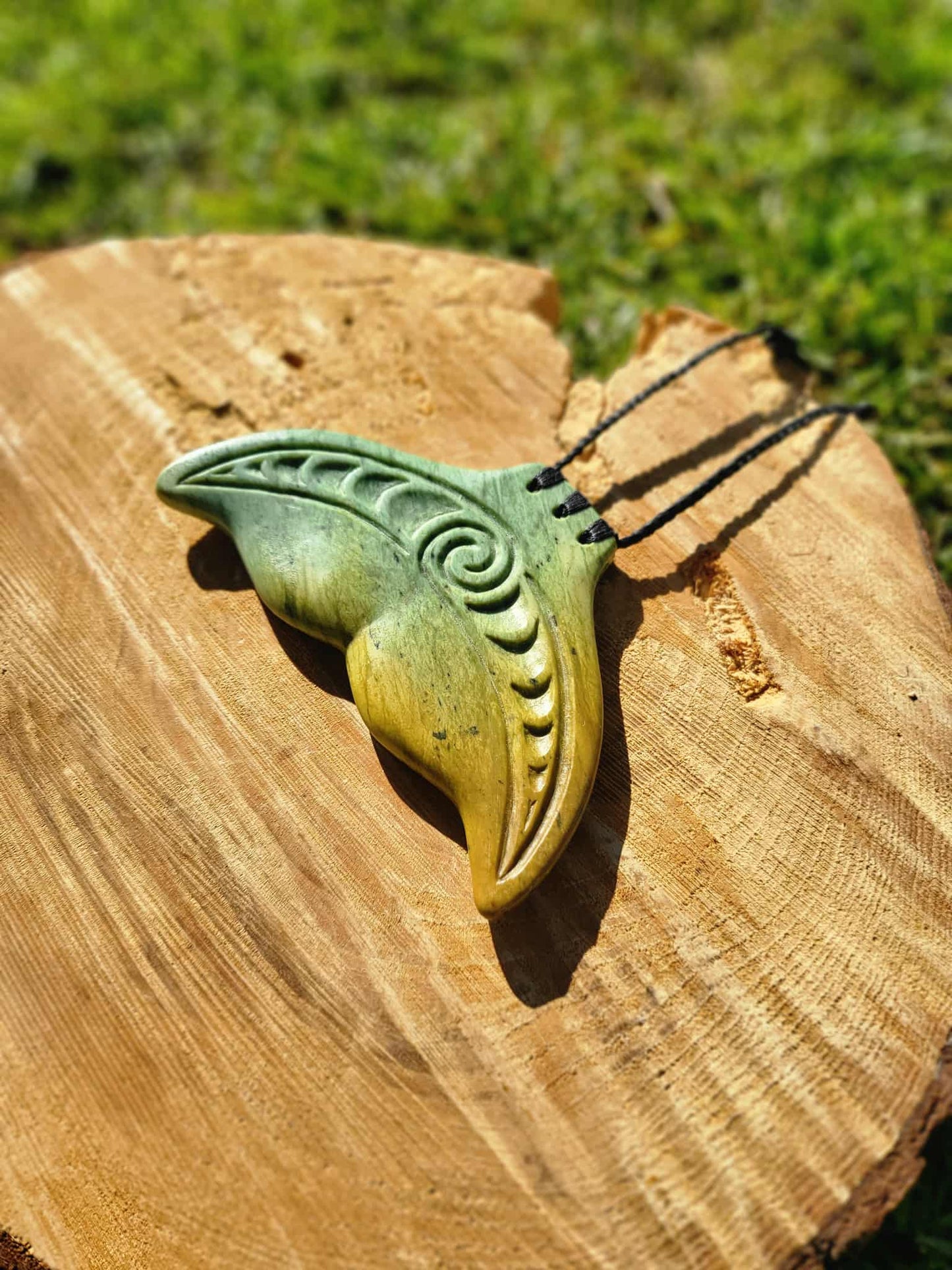 Pounamu (greenstone) muri paraoa (whale tail) necklace on neutral braiding with carved design. Yellow and green variant