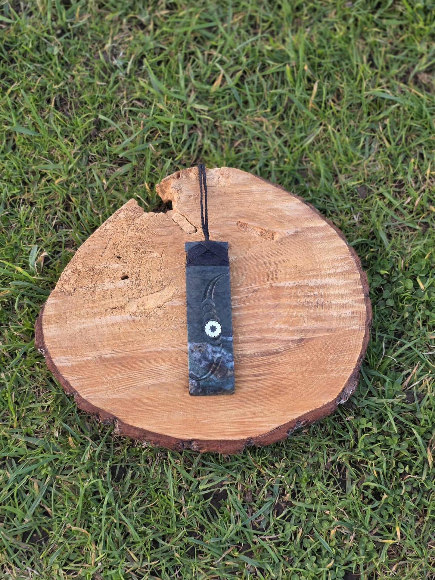 Dark green pounamu greenstone toki (adze) necklace with black strapping, paua and carved decoration
