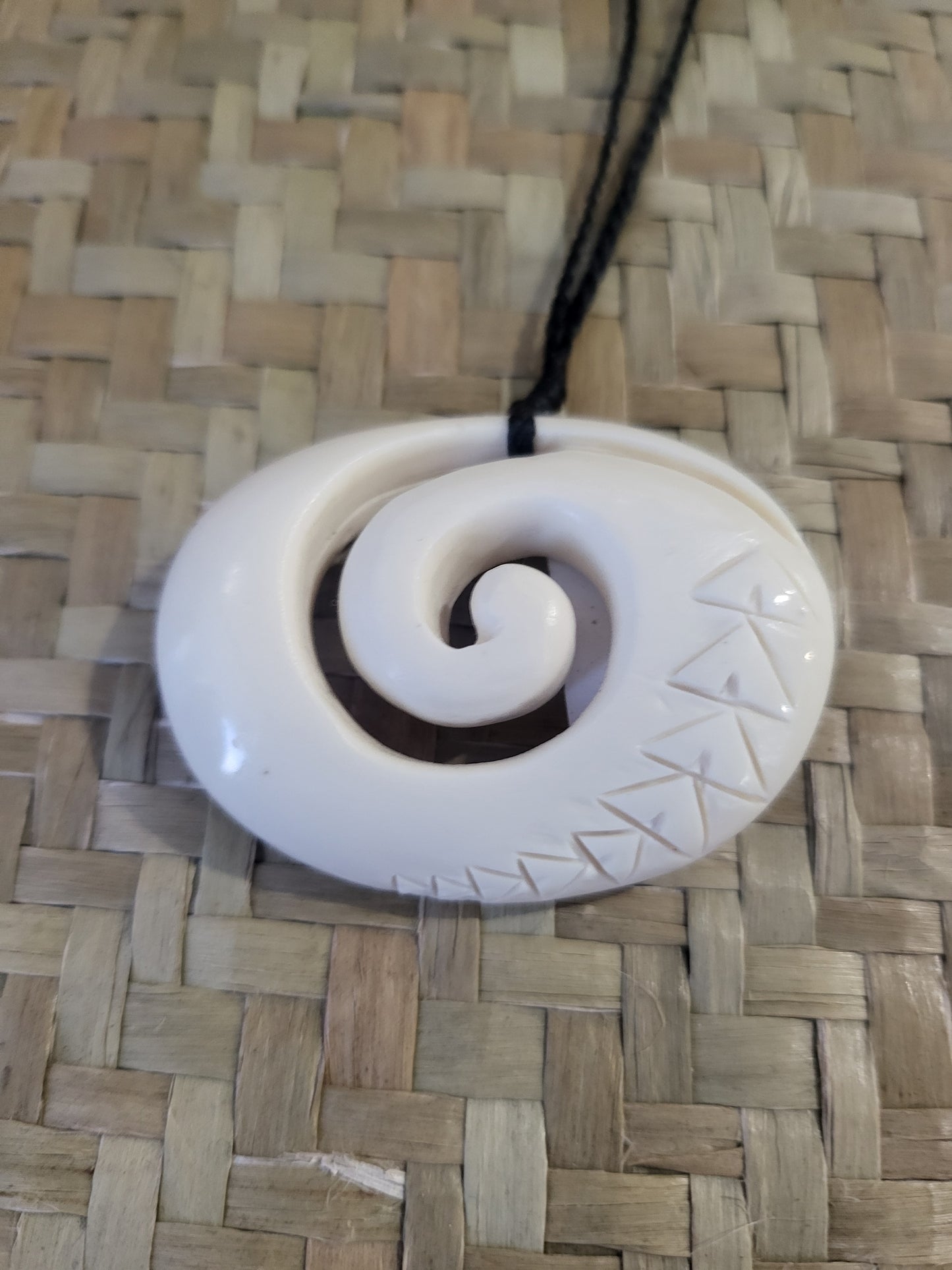 carved bone koru (spiral) necklace on black cord with carved designs