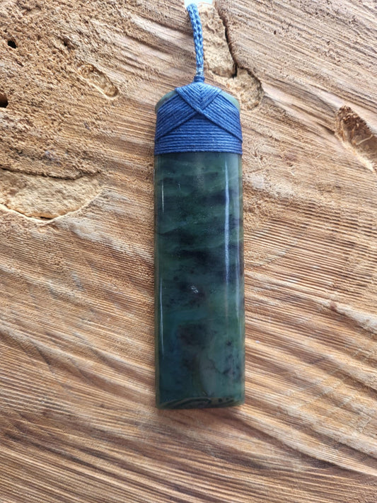 carved pounamu toki (adze) necklace with takarangi (double spiral) carved at the end, on black cord