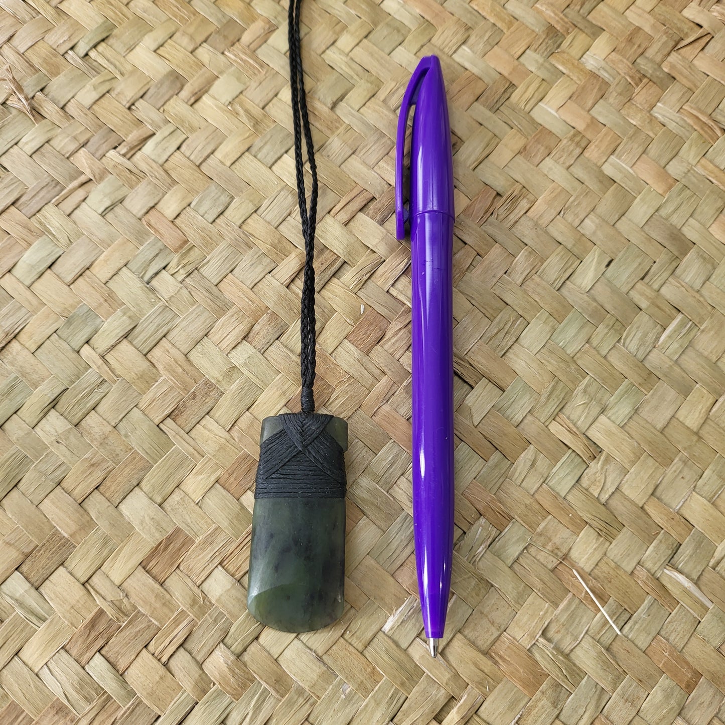 carved pounamu toki (adze) necklace with rounded edge, on black cord