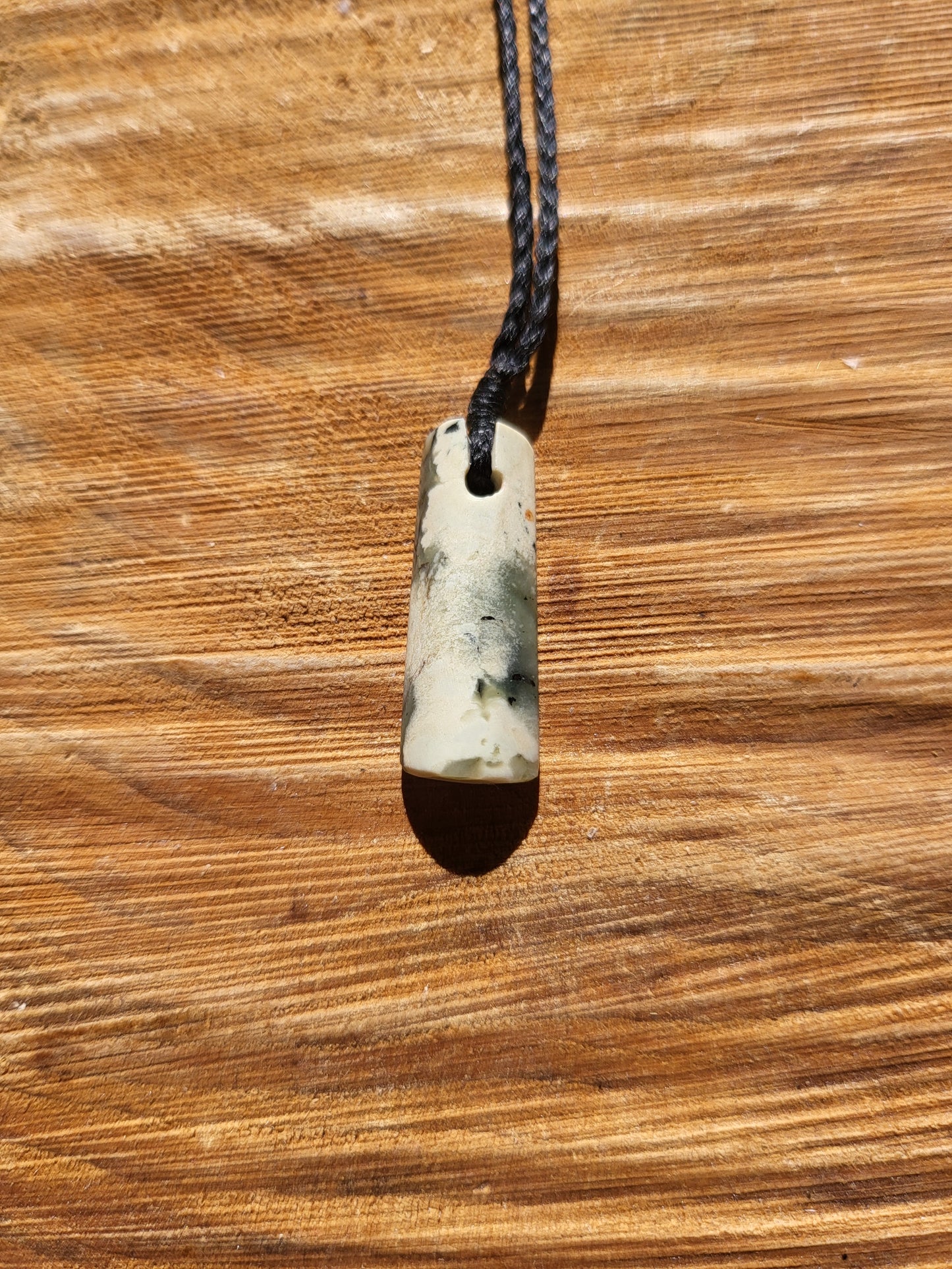 small carved pounamu toki (adze) necklace on black cord, beautiful colour variations within a light green