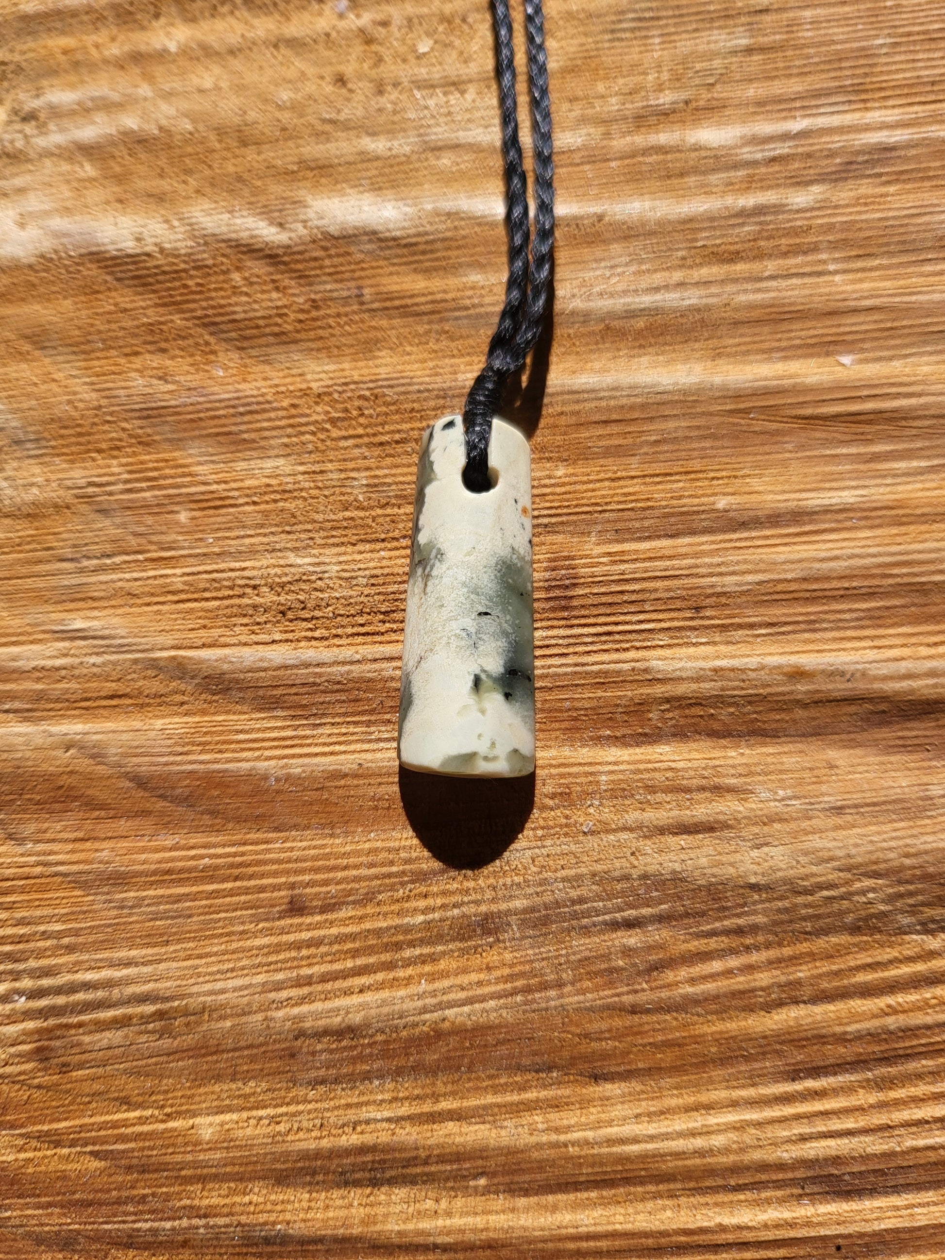 small carved pounamu toki (adze) necklace on black cord, beautiful colour variations within a light green