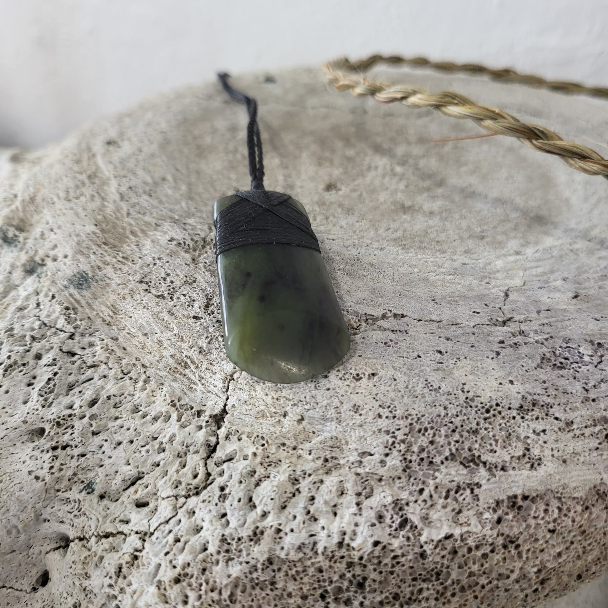 carved pounamu toki (adze) necklace with rounded edge, on black cord