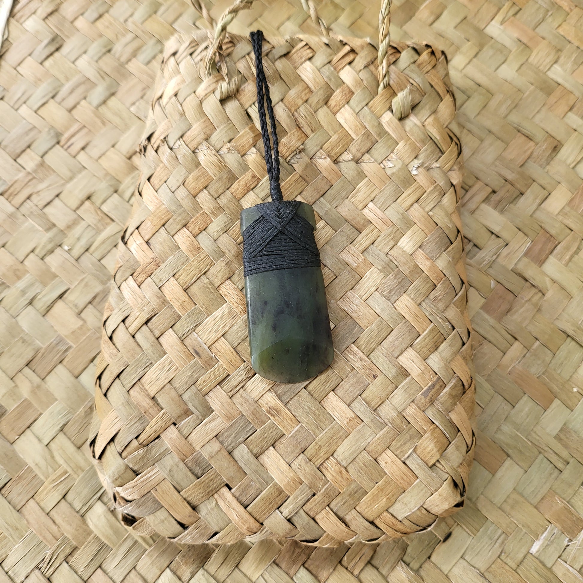 carved pounamu toki (adze) necklace with rounded edge, on black cord