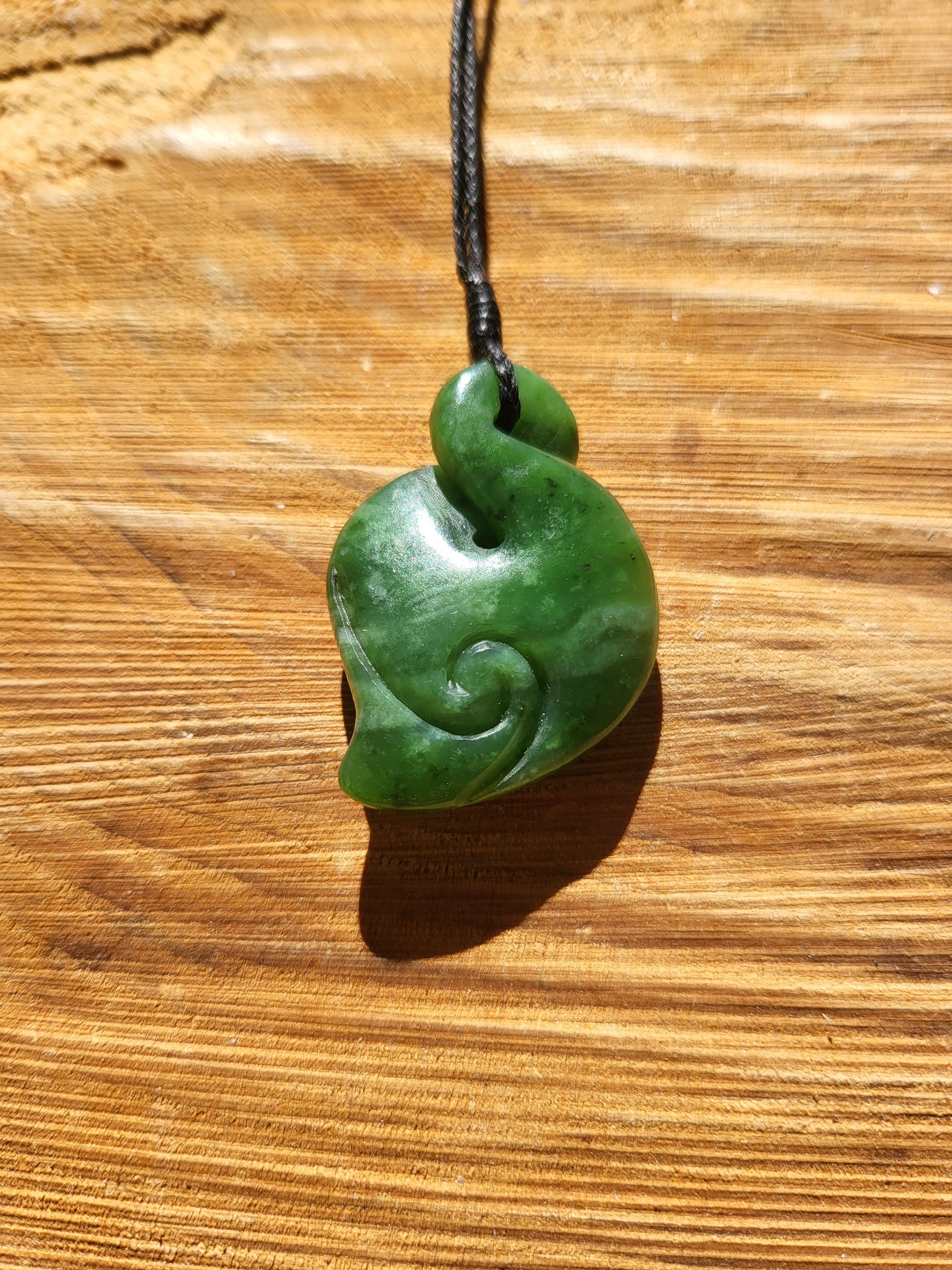 carved pounamu pikorua (double twist) necklace on black cord, beautiful colour variations