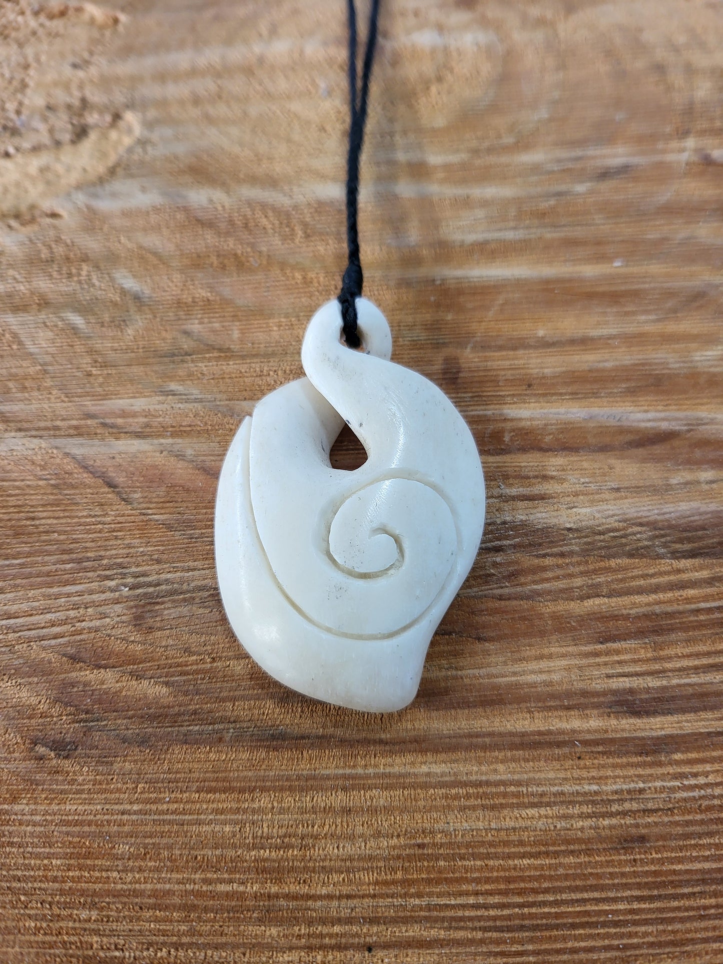carved bone pikorua (double twist) necklace, decorated with koru (spiral) on black cord