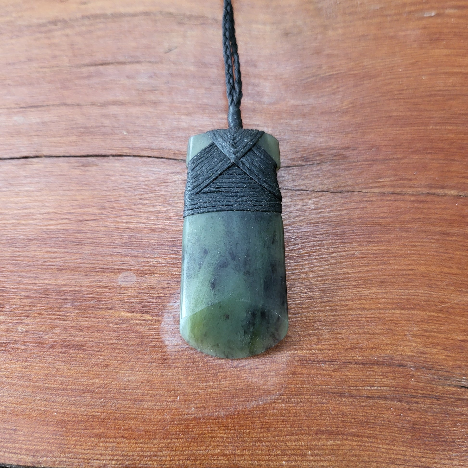 carved pounamu toki (adze) necklace with rounded edge, on black cord